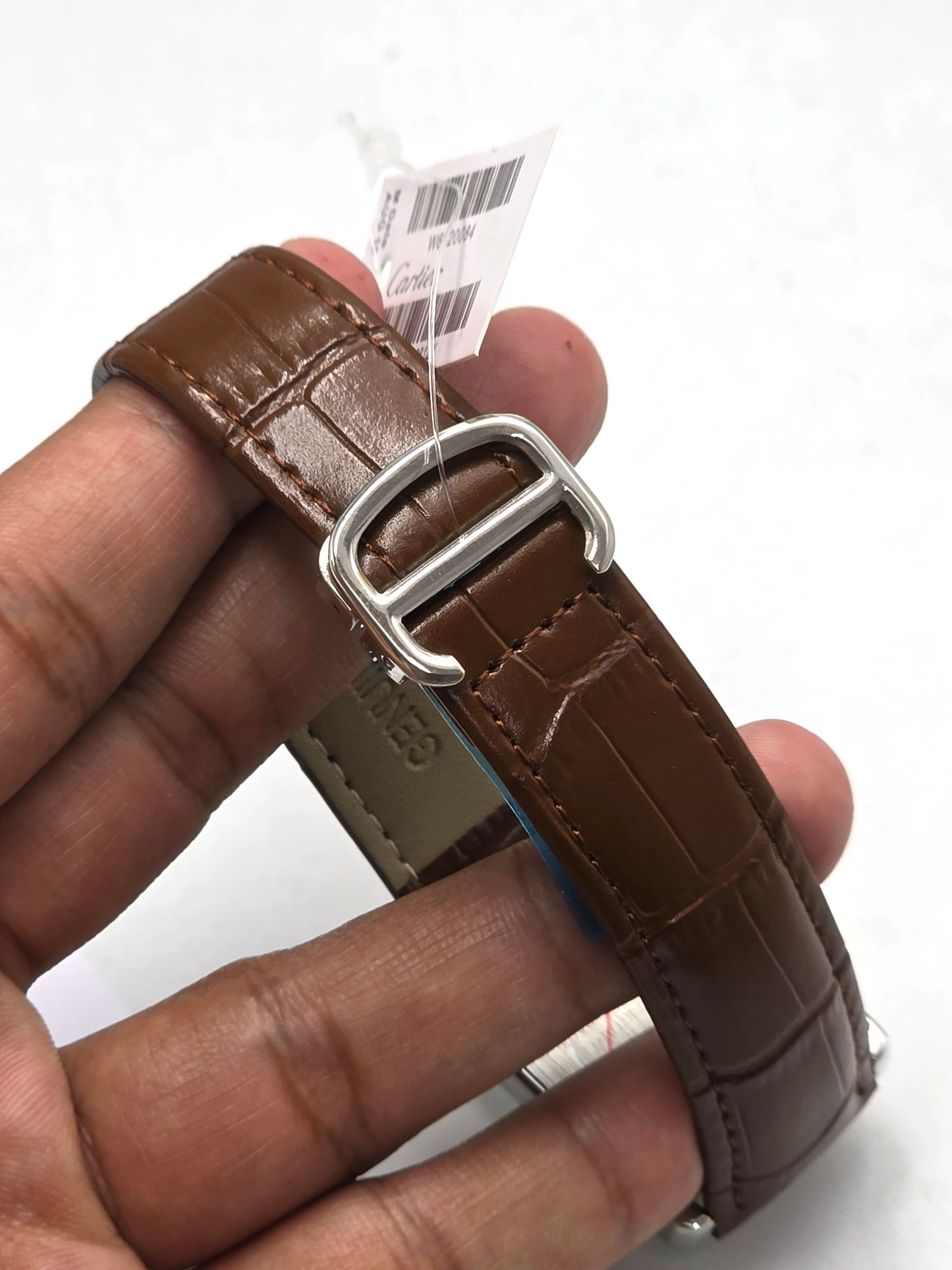 Brown leather watch strap with silver buckle held by a hand on a white background