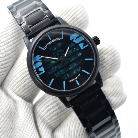 A black stainless steel automatic mechanical watch with a blue dial, held in a gloved hand, with a buckle clasp.