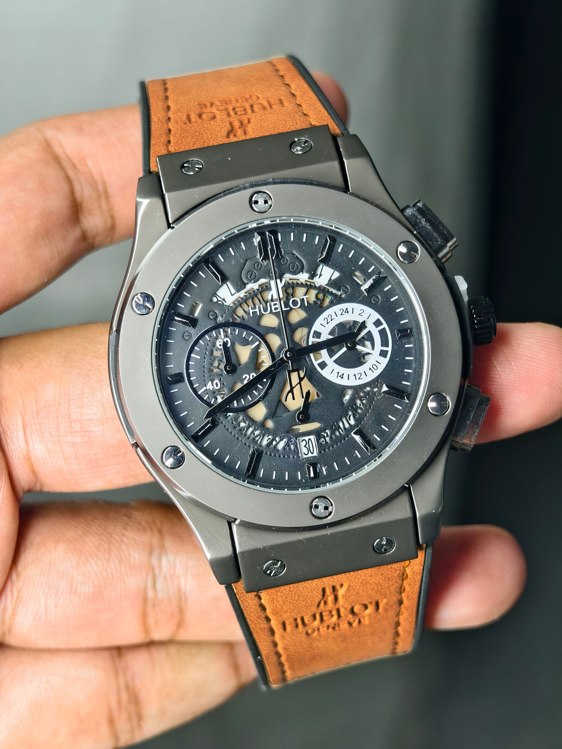 Luxury watch with brown leather strap held in hand against a neutral background